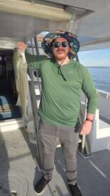 Angler proudly displaying a large Striped Bass aboard the fishing charter, enjoying a sunny day on the water.