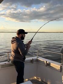 An angler is actively reeling in a catch while fishing on a boat during a scenic sunset.