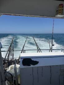 View from the helm of a fishing boat, showcasing multiple fishing rods and the wake left behind as it moves through the ocean.