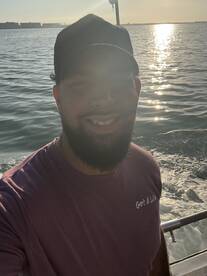 A smiling individual on a boat, with a scenic water background, capturing a moment during a fishing trip.