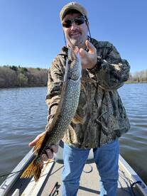Angler proudly displaying a Northern Pike while fishing on a serene lake, showcasing the thrill of freshwater fishing.