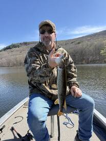 Angler proudly displaying a Northern Pike while fishing on a serene lake surrounded by wooded hills.