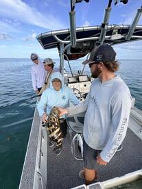 A group of anglers on a boat proudly displaying a large Goliath Grouper during a fishing trip.
