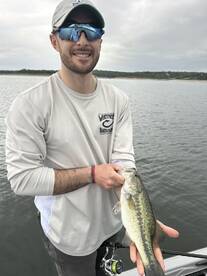 Angler proudly displaying a large Largemouth Bass while fishing on a calm lake.