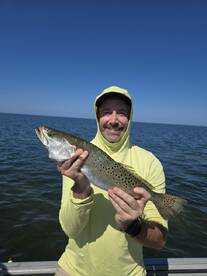 Angler proudly displaying a large Speckled Trout while fishing on a boat in open waters.