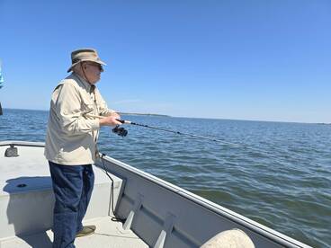 An elderly angler casting a line from a small boat in calm waters, enjoying a peaceful day of fishing.