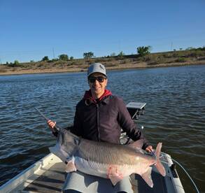 Angler proudly displaying a large Catfish while fishing on a calm lake.