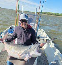Angler proudly displaying a large Catfish while fishing on a boat in a scenic lake environment.