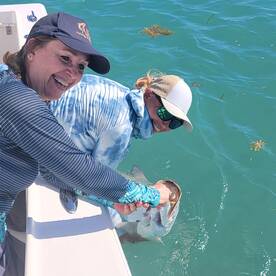 Two anglers joyfully reeling in a fish while enjoying a sunny day on the water.