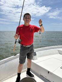 A young angler proudly displaying a caught fish while fishing on a boat in open waters.