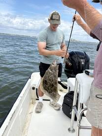 Angler reeling in a Flounder while fishing on a boat, showcasing the excitement of the catch.