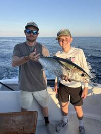 A young angler and an adult proudly displaying a large Tuna on a fishing charter, showcasing their successful catch in open waters.