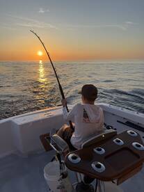 A young angler casting a line into the serene waters at sunset, showcasing a peaceful fishing experience aboard a well-equipped boat.