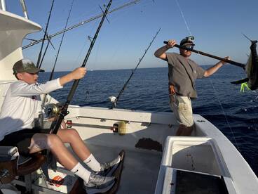 A young angler is actively reeling in a fish while an adult prepares to land a large catch on a deep-sea fishing trip.