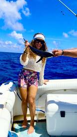 Angler proudly displaying a small fish while aboard a boat in clear blue waters.