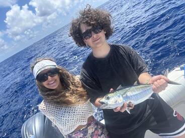 Two young anglers proudly displaying a freshly caught fish while enjoying a day out on the open ocean.