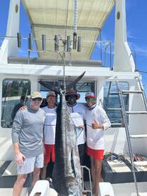 A group of anglers proudly displaying a large Blue Marlin on a fishing charter, showcasing a successful day out on the water.