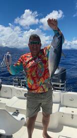 Angler proudly displaying a large fish while fishing on a boat in clear blue waters.