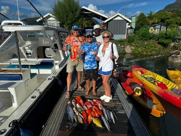 A group of anglers proudly displaying their catch of colorful fish, including Snapper and Mackerel, at the dock after a successful fishing trip in Seychelles.