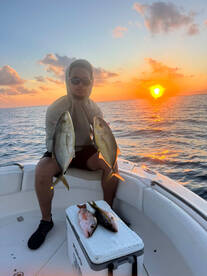 Angler holding two Yellowtail Snapper against a stunning sunset backdrop while fishing from a boat.