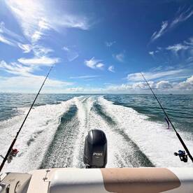 A scenic view from the back of a boat, showcasing the wake and fishing rods against a clear blue sky, perfect for a day on the water.