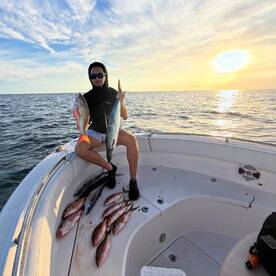 Angler proudly displaying a large Mahi Mahi and Snapper while seated on the boat, with a beautiful sunset backdrop.