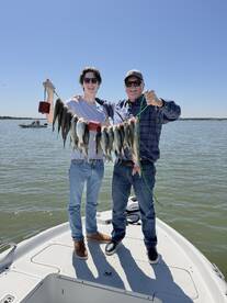 Two anglers proudly displaying their catch of multiple fish while enjoying a sunny day on the water.