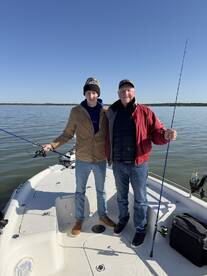 A father and son enjoying a fishing trip together on a boat, both holding fishing rods with a calm water backdrop.