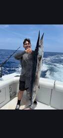 Angler proudly displaying a large Wahoo aboard a fishing boat in open waters.