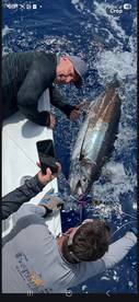 Two anglers actively reeling in a large fish, showcasing the excitement of deep-sea fishing.