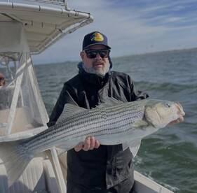 Angler proudly displaying a large Striped Bass while aboard a fishing boat, showcasing a successful day on the water.
