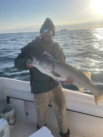 Angler proudly displaying a large Striped Bass while fishing on a boat in open waters.