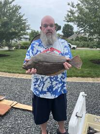 An angler proudly displaying a large Flounder in a residential yard, showcasing a successful fishing trip.
