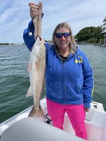 A proud angler holding a large Redfish while on a fishing trip, showcasing the catch against a scenic water backdrop.
