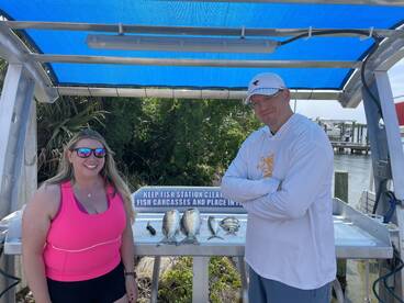 Two anglers proudly displaying their catch of fish at a cleaning station near the dock, enjoying a sunny day on the water.