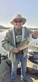 Angler proudly displaying a striped bass while fishing on a calm lake, showcasing a relaxed outdoor experience.