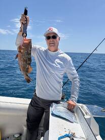 Angler proudly displaying a large Grouper while fishing on a sunny day in open waters.