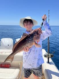 A young angler proudly displaying a large Grouper while fishing on a boat in clear blue waters.