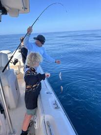 A young angler and an adult are actively fishing on a boat, with multiple fish being reeled in during a sunny day on the water.