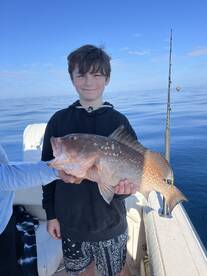 A young angler proudly displaying a large Grouper while fishing on a calm day at sea.