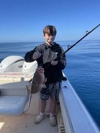 A young angler proudly reeling in a large fish while fishing on a boat in calm waters.