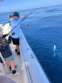 A family enjoying a fishing trip on a boat, with an angler reeling in a fish from the clear blue waters.