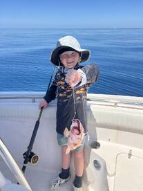 A young angler proudly displaying a freshly caught fish while fishing on a boat in calm waters.