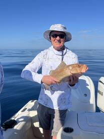 An angler proudly displaying a large Snapper while fishing on a calm day at sea.