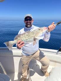 Angler proudly displaying a large Grouper while fishing on a sunny day in open waters.