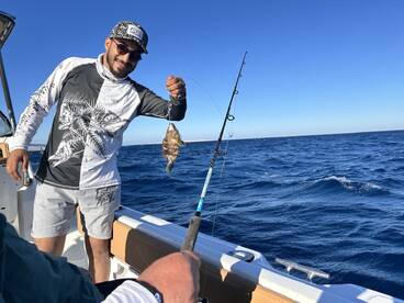 Angler proudly displaying a colorful fish while fishing on a boat in open waters.