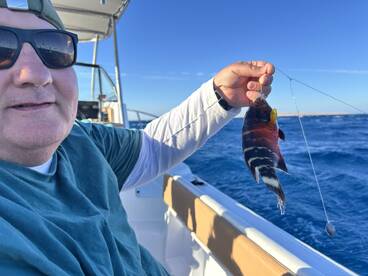 Angler holding a colorful fish while fishing on a boat, showcasing a successful catch in clear blue waters.