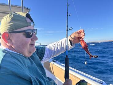 Angler reeling in a vibrant Red Snapper while fishing offshore, showcasing the excitement of the catch.
