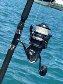 Close-up of a high-quality fishing reel mounted on a rod, set against a vibrant blue water backdrop.