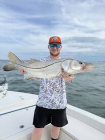 Angler proudly displaying a large Snook while fishing from a boat in coastal waters.